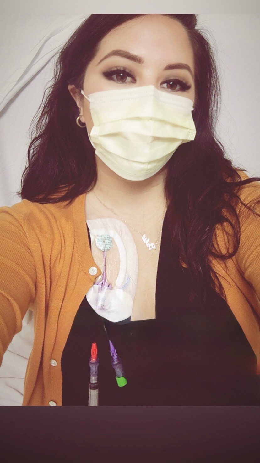 Amanda, masked, takes a selfie showing the central line taped to her chest.